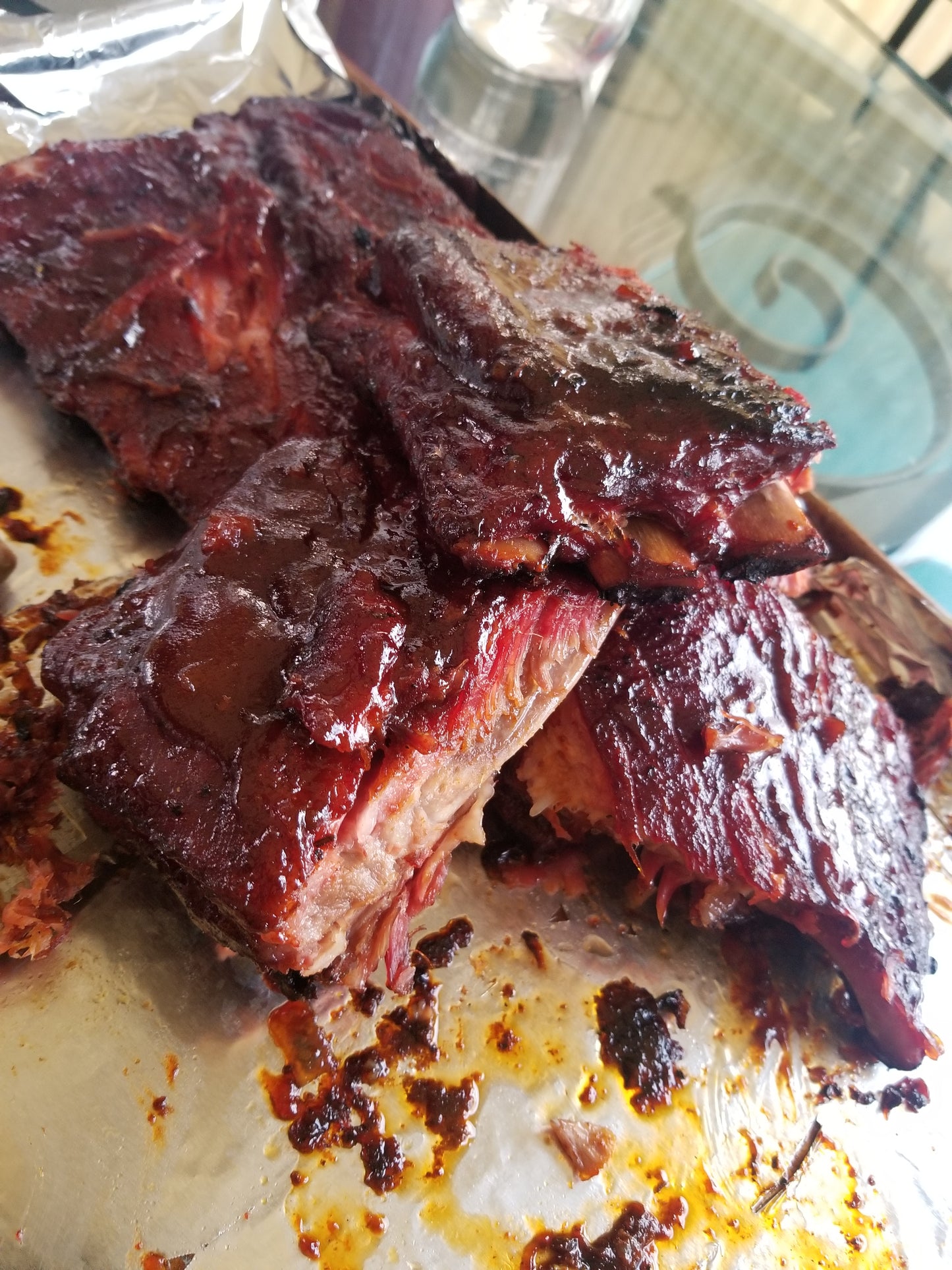 Delicious BBQ ribs being grilled to perfection on an outdoor barbecue. The meat is beautifully charred and covered in a flavorful sauce. A plume of mouthwatering smoke rises from the grill. Perfect BBQ for a summer gathering.